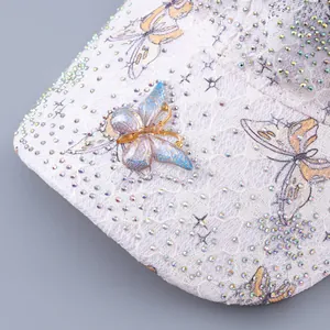 Detailed view of white lace baseball cap featuring iridescent rhinestones and enamel butterfly