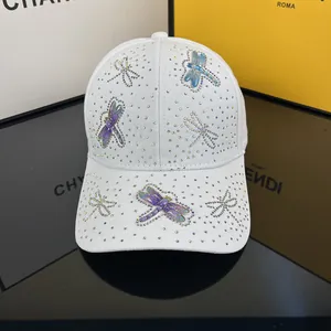 White baseball cap with colorful rhinestones and crystal dragonflies on a glossy surface