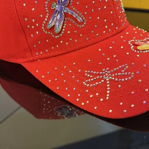 Detail of red rhinestone baseball cap with purple dragonfly ornament and canvas texture