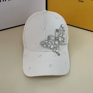 Detailed view of a white baseball cap featuring rhinestone butterfly and pearl accents