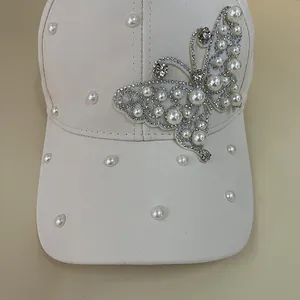 Detailed view of cream baseball cap featuring pearl butterfly patch and rhinestone accents