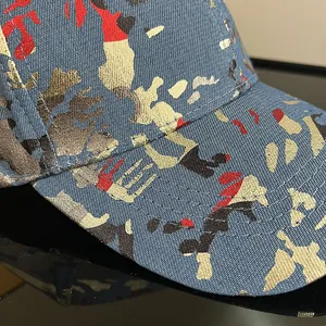 Detail shot of blue denim fabric with metallic gold camo print and stitching on hat brim