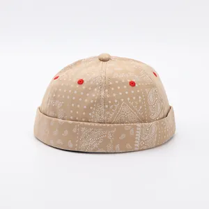 Dettaglio ravvicinato del cappello docker beige con motivi paisley bianchi e occhielli