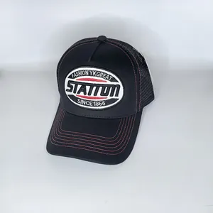 Detail der schwarzen Mesh-Trucker-Kappe mit weißer Stickerei und roten Kontrastnähten