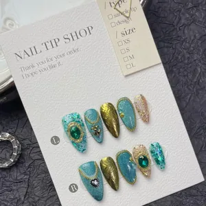 Detailed view of handmade long almond cat-eye nails with emerald gems and gold relief