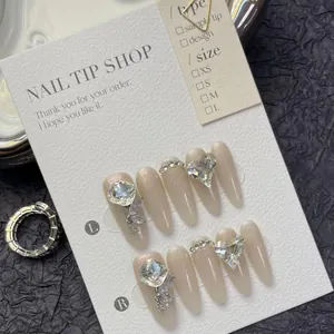 Macro di unghie finte stiletto lunghe con glitter dorati, strass a cuore e charms a farfalla