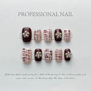 Dettaglio di unghie finte tweed rosse e crema con decorazioni floreali in perle e strass