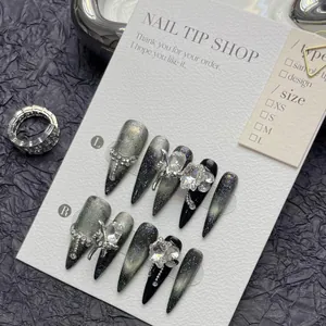 Macro detail of dark cat-eye stiletto press-on nails with 3D bows and silver chains