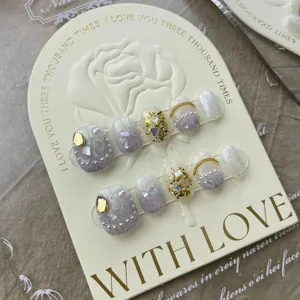 Detail of luxury handmade press-on nails with pearls, gold foil, and crystals on a display card