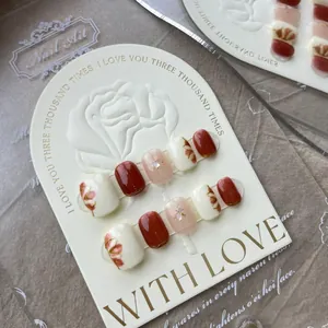 Macro detail of handmade burgundy and cream press-on nails with gold floral foil and rhinestones