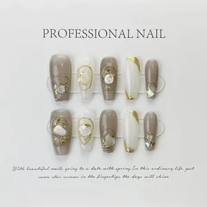 Detail of handmade press-on nails featuring nude and milky tones with gold foil and shells