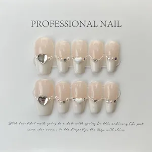 Close-up of handmade press-on nails with white pearls, rhinestones and heart relief details