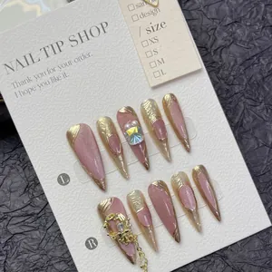 Pink cat eye press-on nails with gold edges and crystal charms on a display card