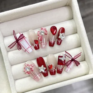 Faux ongles faits main longs à la française avec nœuds rouges, strass et carreaux
