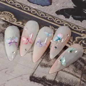 Gros plan de stickers ongles papillon avec perles et strass sur base de dégradé rose