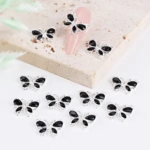 Detailed view of silver butterfly nail charms with black crystals on almond-shaped nails
