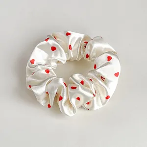 Dettaglio di un elastico per capelli in raso bianco perla con piccoli cuori rossi