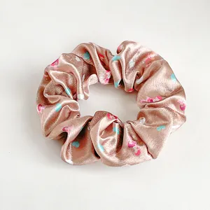 Dettaglio dell'elastico scrunchie in satin champagne con cuori colorati e trama di seta