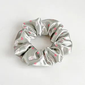 Dettaglio di un grande elastico in raso argento con cuori rosa e motivi di gatti