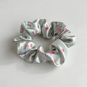 Dettaglio di scrunchie in raso con unicorno arcobaleno e motivi a cuore rosso su argento