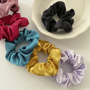 Detail of satin scrunchies in multiple colors with silk-like gloss and wavy porcelain plate