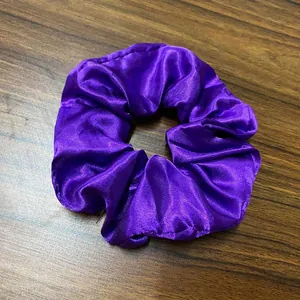 Detailansicht eines dunkelvioletten Satin-Haargummis mit LED auf dunklem Holzgrund