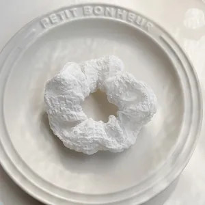 Dettaglio dell'elastico per capelli bianco con trama a bolle su piatto di ceramica