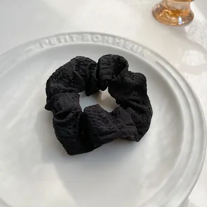 Dettaglio macro dello scrunchie nero in tessuto plissettato con bordi a balze su piatto
