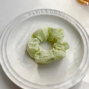 Dettaglio di uno scrunchie verde chiaro in tessuto testurizzato su vassoio di ceramica