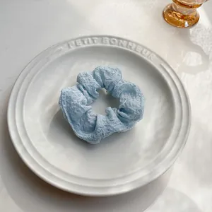 Dettaglio scrunchie in seersucker celeste con trama a nuvola su un piatto di ceramica bianca