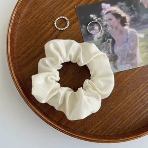 Nahaufnahme eines cremefarbenen Satin-Scrunchies auf einem Holztablett mit Karten