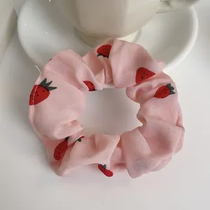 Dettaglio scrunchie in chiffon con stampa a fragole su tavolo bianco con tazzina