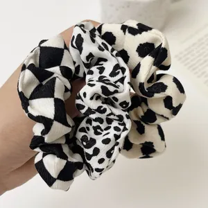 Detail shot of leopard print, cow pattern and checkerboard fabric scrunchies held by hand