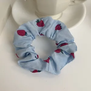 Dettaglio dello scrunchie in chiffon azzurro con stampa di fragole su una tazzina