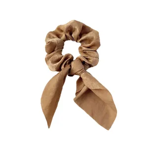 Détail d'un chouchou en satin marron avec un nœud et de longs rubans sur blanc