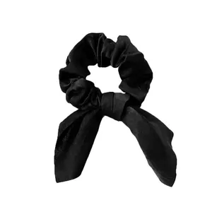 Détail d'un chouchou en satin noir avec nœud décoratif et texture de tissu lisse et brillant
