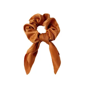 Détail de la texture satinée et du ruban oreille de lapin du chouchou couleur caramel soyeux