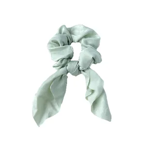 Détail d'un chouchou en satin vert clair avec grand nœud et tissu texturé doux
