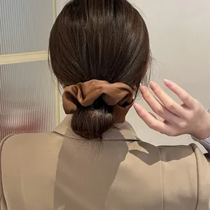 Detailopname van een bruine satijnen scrunchie in een lage knot met beige blazer