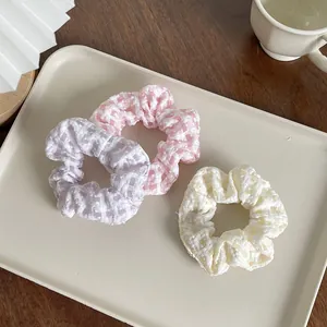 Detailed view of plaid fabric scrunchies in pastel purple, pink and cream colors