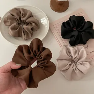 Detailweergave van vier luxe satijnen scrunchies in bruin, zwart en beige zijdeglans