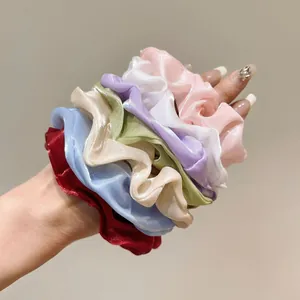 Dettaglio di sette elastici scrunchie in organza pastello indossati al polso per misura
