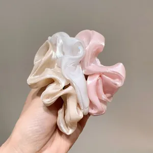 Dettaglio di tre elastici in organza champagne, bianco e rosa con texture perlata