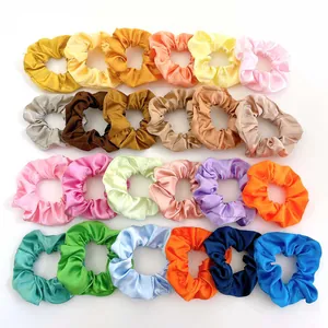 Flat lay of 24 colorful satin hair scrunchies in various shades on a white background