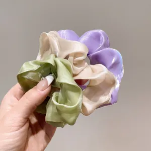 Dettaglio di tre elastici per capelli in organza verde, oro e viola sulla mano