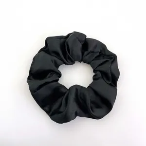 Close-up of black satin scrunchie showing smooth silk-like texture and detailed fabric folds