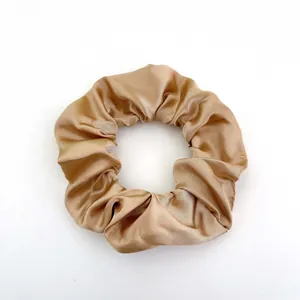 Detailed view of champagne gold satin scrunchie showing glossy texture and soft folds