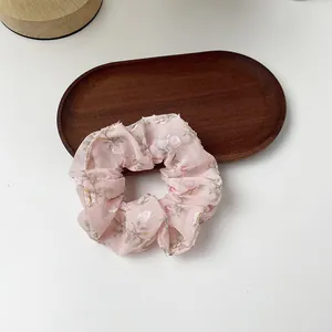 Close-up of pink floral organza scrunchie with silver threads on a wooden tray