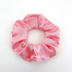 Macro view of silky light pink satin scrunchie with soft fabric pleats on white background