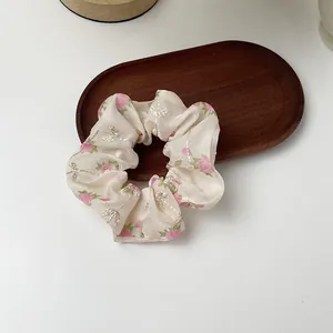 Close-up of floral organza scrunchie with pink rose patterns and silver embroidery